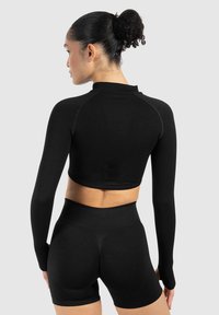 Sort cropped langærmet top med ribbet tekstur og mock neck, parret med højttaljede sorte shorts med en glat finish.