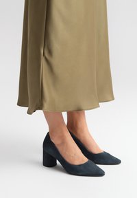 Décolleté in suede blu navy con punta affusolata e tacco largo a blocco, abbinati a una gonna fluida in satin verde oliva.