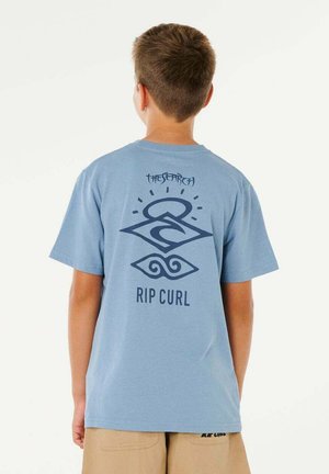 Garçon portant un t-shirt Rip Curl bleu clair avec un graphique noir et le texte "THE SEARCH" au dos, associé à un short beige.