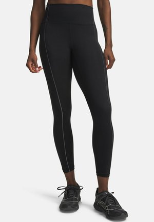 Zwarte leggings met hoge taille en zichtbare zijnaden, gedragen door een persoon, gecombineerd met zwarte sportschoenen op een witte achtergrond.