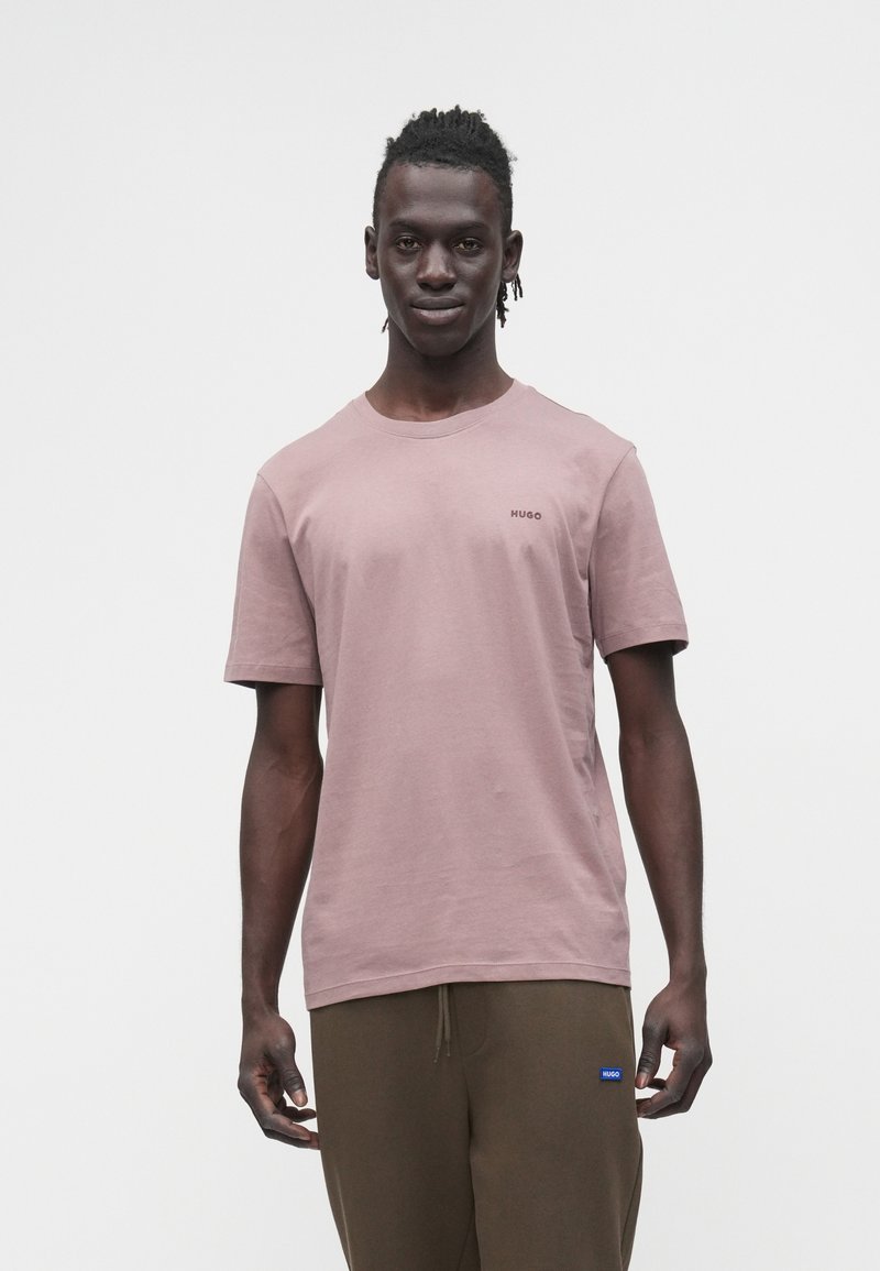 Tricou roz din bumbac, cu mâneci scurte și decolteu rotund, având un mic logo "HUGO" pe partea stângă a pieptului. Textură fină, design simplu.