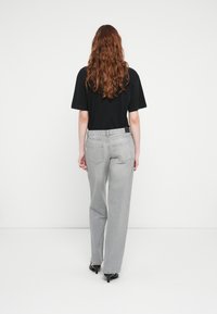 Black oversized t-shirt, gray high-waisted jeans, straight-leg design, five pockets, and black high-heeled shoes. Back view.