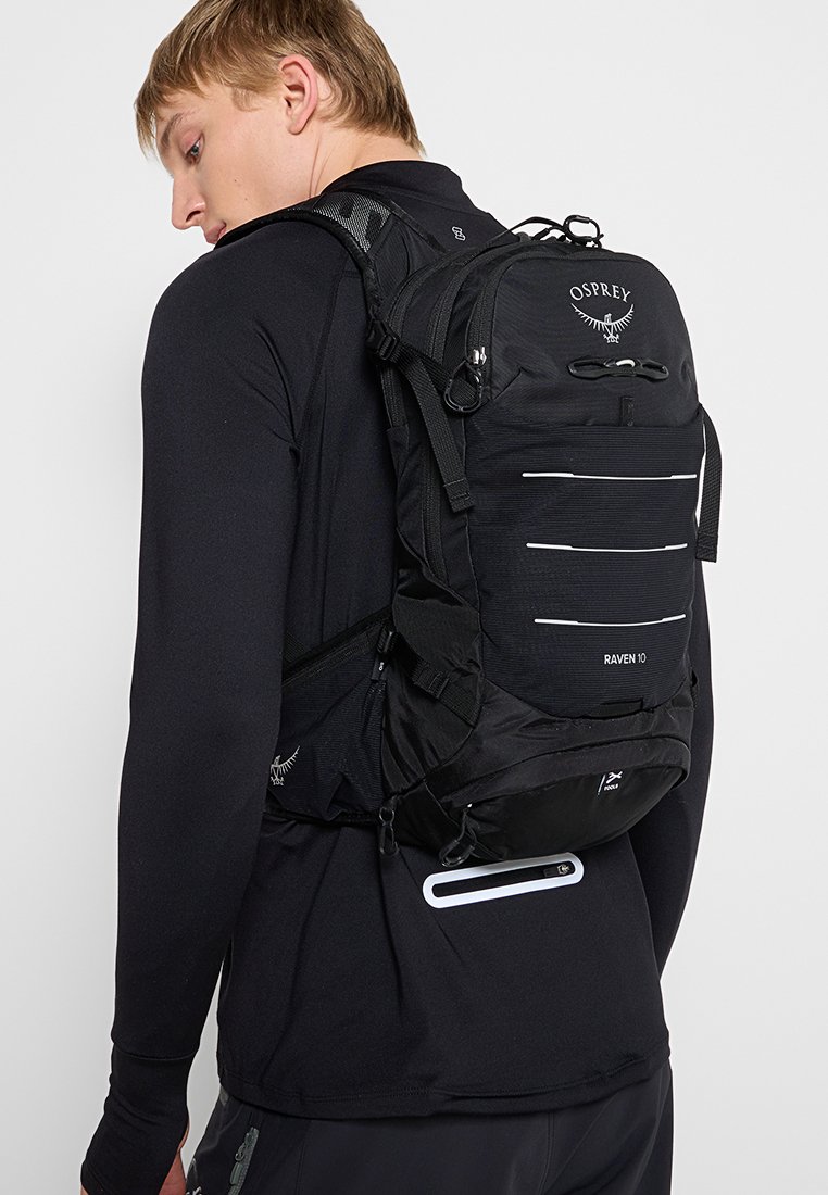 Mochila Black Osprey Raven 10 con múltiples bolsillos frontales, correas laterales y acentos reflectantes, que presenta un diseño técnico y elegante.