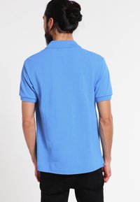 Polo bleu en tissu texturé, avec un col classique et des manches courtes, associé à un pantalon noir.