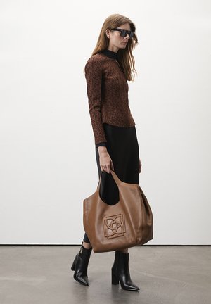 Bruin panterprint langemouwtop, zwarte broek, oversized bruine leren tas met ingegraveerd patroon, zwarte puntige enkelboots.