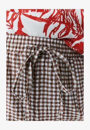 Brązowe i białe szorty w kratkę z elastycznym pasem i zawiązywanym sznurkiem. Czerwony nadrukowany top częściowo widoczny powyżej szortów.