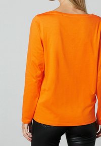 Langärmliges oranges T-Shirt mit Rundhalsausschnitt, aus einem weichen Material gefertigt; hat eine glatte Textur und eine lockere Passform.