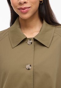 Olive green button-up jacket with a collar, featuring two buttons and smooth, textured fabric. Includes visible stitching details.