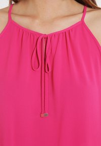 Pink sleeveless top featuring a gathered neckline with drawstrings and a metallic accent at the end of the ties. Smooth texture.