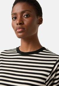 Koszulka w paski z czarno-białymi poziomymi paskami, okrągłym czarnym dekoltem, krótkimi rękawami i miękką fakturą tkaniny.