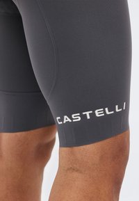 Κοντινό πλάνο σκούρων γκρι σορτς ποδηλασίας με το λογότυπο "Castelli" στο μηρό, φορεμένα από άτομο με καστανό χρώμα δέρματος.