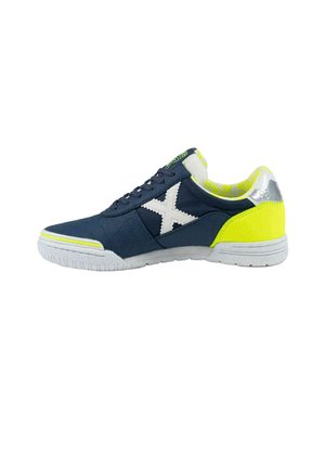 Zapatilla deportiva azul marino con suela blanca, X lateral blanca, talón y forro interior amarillo neón, y cierre con cordones, mostrada de perfil sobre fondo blanco.