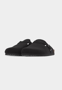 Paar schwarze Slip-on-Clogs mit geschlossenem Zehenbereich, verstellbarem Schnallenriemen und profilierter Sohle vor weißem Hintergrund.