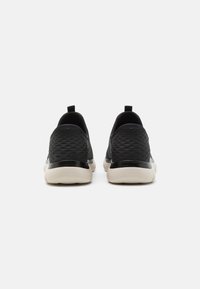 Black slip-on sneakers with a textured upper, rounded toe, and lightweight cream sole. Features a pull tab at the heel for easy wear.