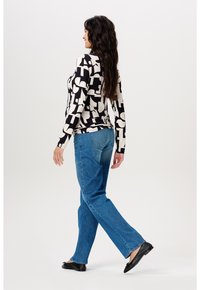 Langärmliges Oberteil in Creme mit einem auffälligen schwarzen geometrischen Muster, kombiniert mit hellblauen geraden Jeans und schwarzen Flats.
