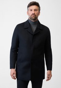 Heren donkerblauwe jas, gemaakt van wol, voorzien van een notch-kraag, twee zijzakken en een rechte snit, gedragen over een grijze coltrui.