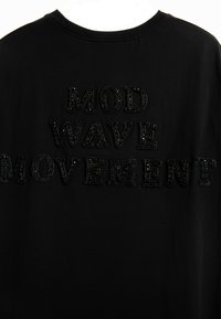 Camiseta negra con texto texturizado y en relieve en negro que dice "MOVIMIENTO MOD WAVE" en la parte posterior. Tela suave, cuello redondo.