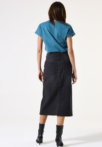 Jupe midi en denim noir avec poches arrière, taille haute et silhouette droite. Associée à une chemise à manches courtes teal et des bottines noires.
