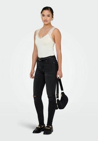 Hvid tanktop med blonder, sorte skinny jeans med revner på knæene, sorte loafers med guldkæde og en lille sort skuldertaske.