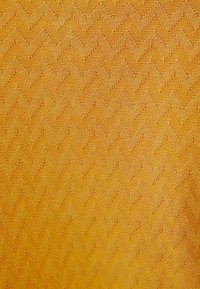 Tkanina zygzakowata w intensywnych odcieniach żółci i pomarańczy, charakteryzująca się fakturowaną powierzchnią, która dodaje głębi i wymiaru.