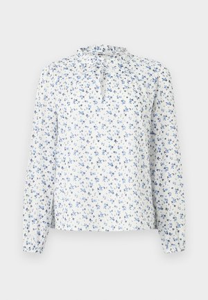 Blouse blanche à manches longues avec motif floral bleu, col à volants et détail noué à l'avant.