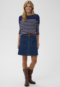 Gestreifter Marine- und Beigepullover aus Strick, kombiniert mit einem Jeans-A-Linien-Rock mit Frontknöpfen und großen Taschen. Brauner Ledergürtel und hohe Stiefel.