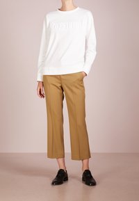 Sudadera blanca con el logo "HUGO" en relieve, combinada con pantalones anchos color tostado y zapatos negros, presentada sobre un fondo pastel.