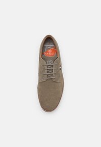 Zapato marrón de ante perforado con cordones y suela de goma, que presenta un logo en el lateral y una etiqueta de plantilla naranja que dice "bugatti".