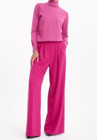 Fuchsiarosa stickad polotröja kombinerad med vida fuchsiarosa byxor. Mjuk textur, hög midja och veckade designdetaljer.