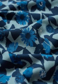 Țesătură din bumbac cu un model floral în nuanțe de albastru pe un fundal teal deschis. Textura pare moale și ușor șifonată.