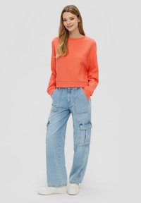 Sweatshirt court texturé corail à manches longues associé à un pantalon cargo clair à jambe large et des baskets blanches.