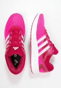 Scarpe da ginnastica rosa con parte superiore in mesh, strisce bianche e colletto imbottito. Presentano una suola spessa bianca e sovrapposizioni testurizzate per supporto.