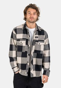 Black and white checkered flannel shirt with two chest pockets, button-down front, and a plain white t-shirt underneath. Classic design.