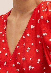 Tissu rouge avec un motif floral blanc ; design en v-cou et manches courtes, présentant une texture douce et une coupe ample.
