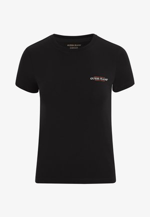 Svart bomull t-skjorte med korte ermer, rund hals, og en liten rød og hvit "GUESS JEANS" logo på venstre bryst. Glatt tekstur.