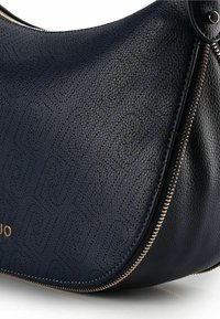 Borsa a mano in pelle blu navy con motivo in rilievo, forma curva e dettagli con cerniere color oro. Finitura strutturata, con un bordo liscio e lucido.