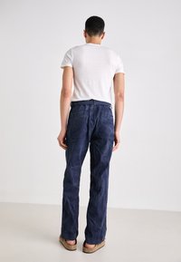 Donkerblauwe denim broek met een recht gesneden ontwerp, voorzien van achterzakken en een gladde textuur, gedragen met een effen wit T-shirt.