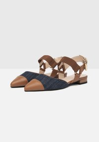 Bailarinas de denim azul con acentos de cuero marrón, diseño de punta afilada y correas ajustables en los tobillos; tacón plano para estabilidad y comodidad.