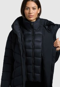 Must coat mustas kõrge kraega, varustatud tõmblukkudega ja quiltitud mustriga. Pehme, kerge materjal, mis on loodud sooja hoidmiseks.