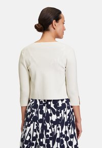 White three-quarter sleeve top with a rounded neckline, paired with a navy and white patterned skirt featuring floral designs.