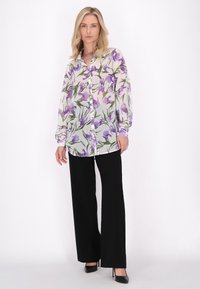 Bluză ușoară, transparentă, cu un model floral în nuanțe de violet și verde, cu nasturi, asortată cu pantaloni largi negri și tocuri negre.