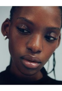 Nærbillede af et ansigt med glat hud, fyldige læber og mørkebrune øjne. Har en subtil glans og små runde sølvøreringen.