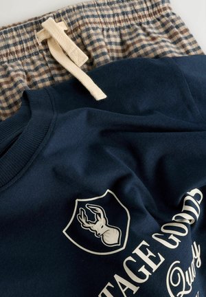 Navy blue sweatshirt with logo and text, paired with brown and beige checkered pajama shorts featuring a drawstring. Soft cotton material.