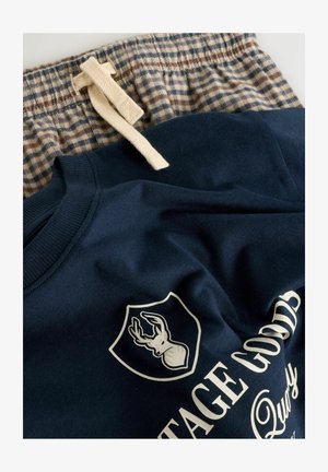 Sweat-shirt bleu marine avec logo et texte, associé à un short de pyjama à carreaux marron et beige avec cordon de serrage. Matière en coton doux.