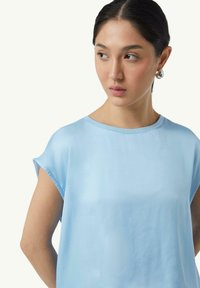 Jasnoniebieski krótki rękaw top o luźnym kroju, z okrągłym dekoltem i gładką fakturą materiału. Prosty design bez widocznych wzorów.