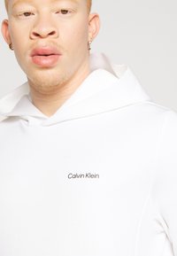 Sweat à capuche blanc avec logo Calvin Klein. Matériau en coton doux mélangé, design minimaliste et coupe décontractée.