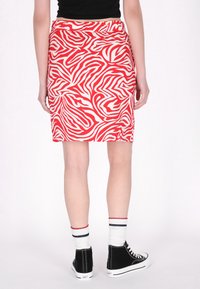 Fustă creion cu model zebra roșu și alb, dintr-un material neted, cu talie medie și tăietură până la genunchi. Asortată cu adidași negri tip high-top.