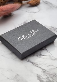 Gråtexturerad smyckeslåda med slät yta och präglad silverlogotyp. Rektangulär form, stängd, vilande på en marmoryta.