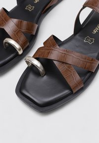 Sandalias de imitación de cocodrilo marrones con tiras cruzadas, acentos metálicos plateados y una textura de suela cuadrada negra.