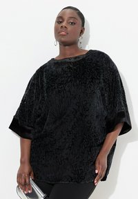 Top in velluto nero con motivo floreale, maniche larghe e scollatura rotonda. Tessuto testurizzato con una morbida lucentezza. Colore profondo e intenso.